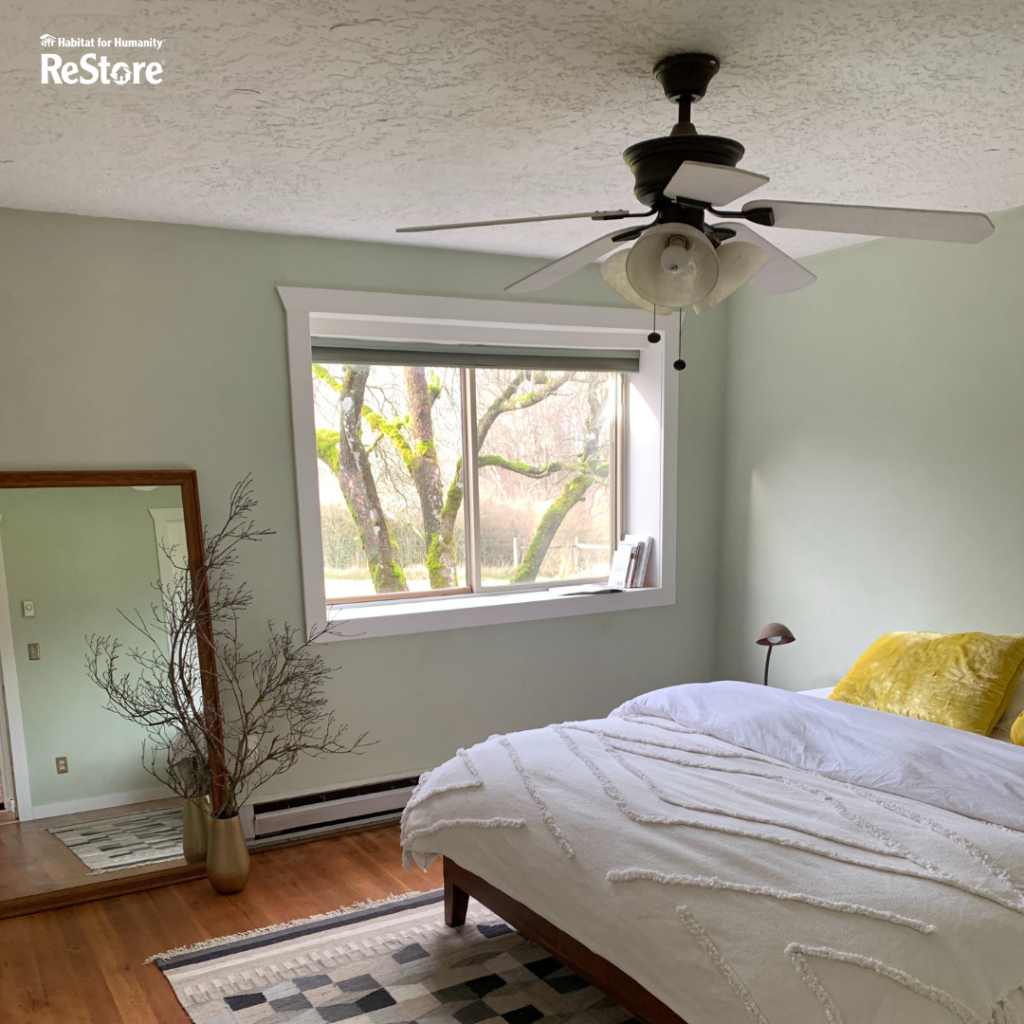A ceiling fan with white shades hanging down from the ceiling of a bedroom with two strings attached to the fan. 
