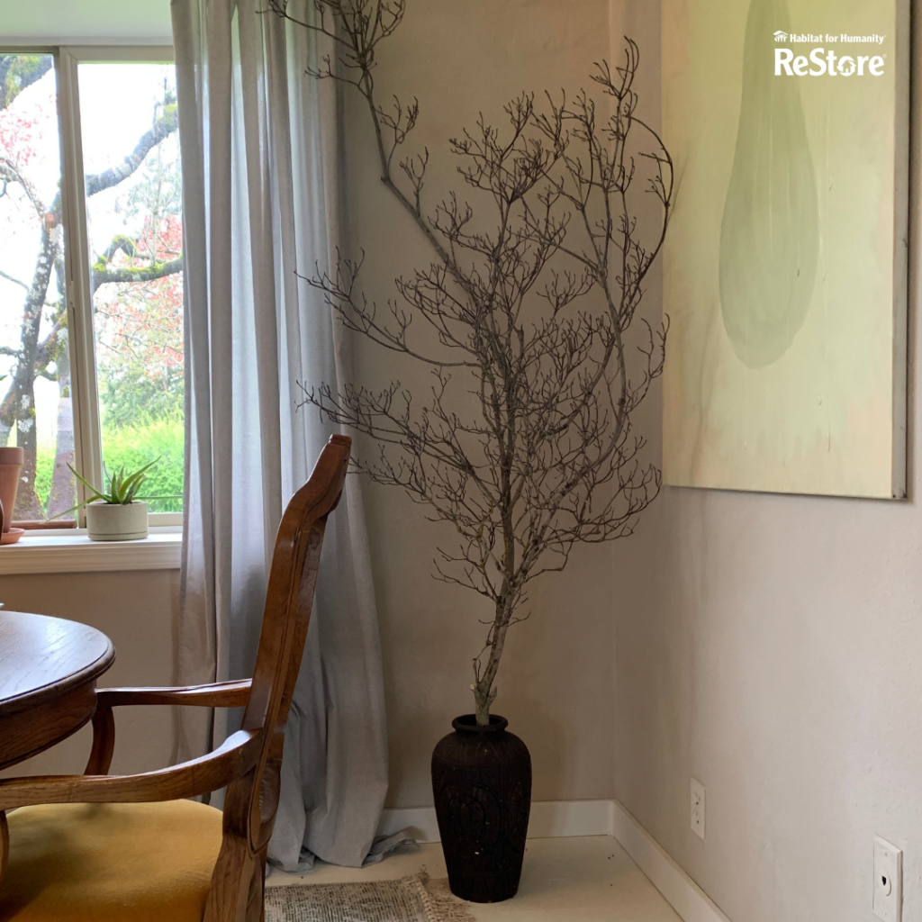 A large black ceramic floor vase sitting against a beige wall with a leafless tree in the vase.