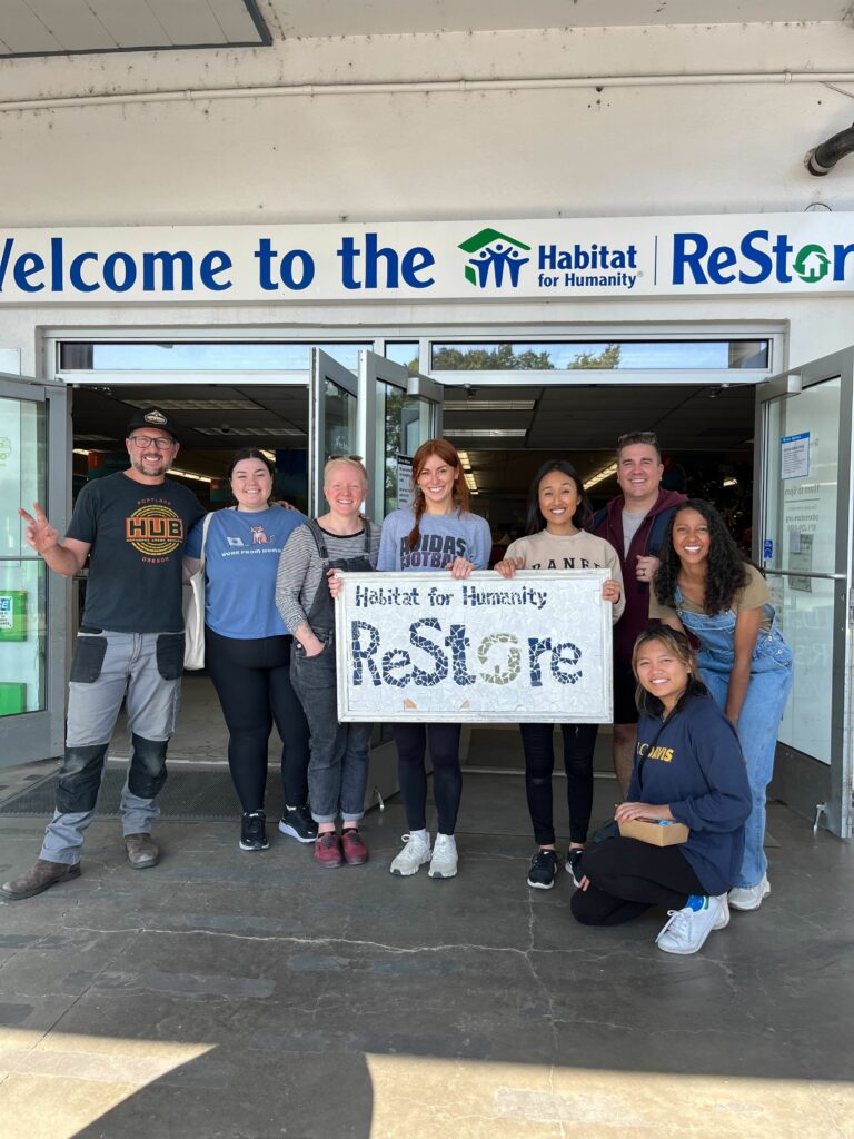 Image of Avenue and Hopworks Brewery staff holding a ReStore sign in front Portland ReStore